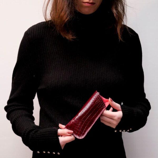 Cette photo représente une jeune femme portant un étui à lunette en cuir rouge façon croco