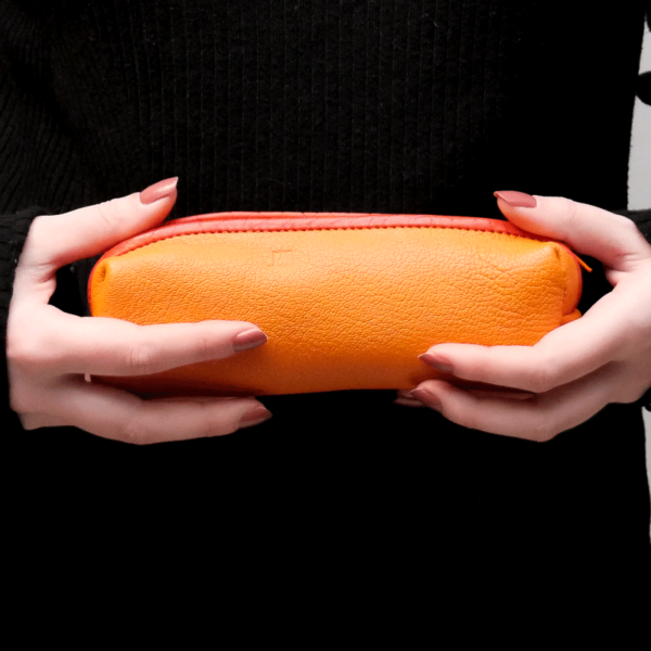 Cette photo montre les mains d'une jeune femme portant une trousse en cuir orange