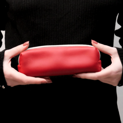 Cette photo montre les mains d'une jeune femme portant une trousse en cuir rouge