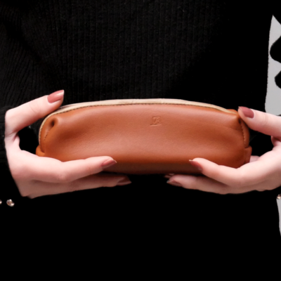 Cette photo montre les mains d'une jeune femme portant une trousse en cuir marron