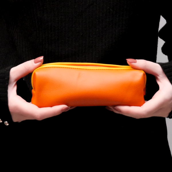 Cette photo montre les mains d'une jeune femme portant une trousse en cuir orange