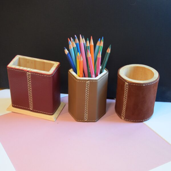 Cette photo représente 3 étuis à crayon en bois recouvert de cuir. Des crayons sont posés dans un des pots