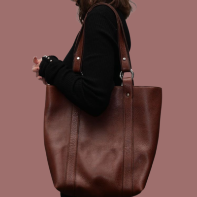Cette image représente une jeune femme portant un grand sac en cuir marron avec 2 anses