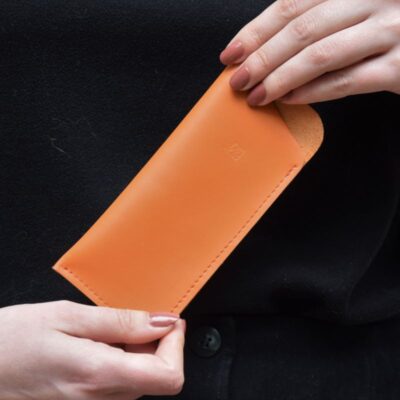 Cette photo représente les mains d'une jeune femme portant un étui à lunette en cuir orange