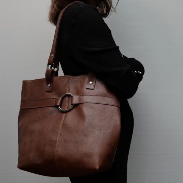 Cette image représente une jeune femme portant un grand sac en cuir marron avec 2 anses et une grande boucle
