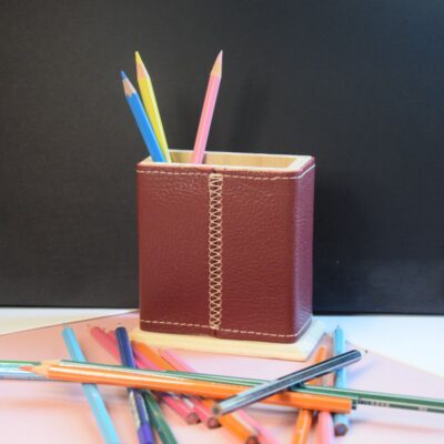 Cette photo représente un étui à crayon en bois recouvert de cuir bordeaux Des crayons sont posés à côté