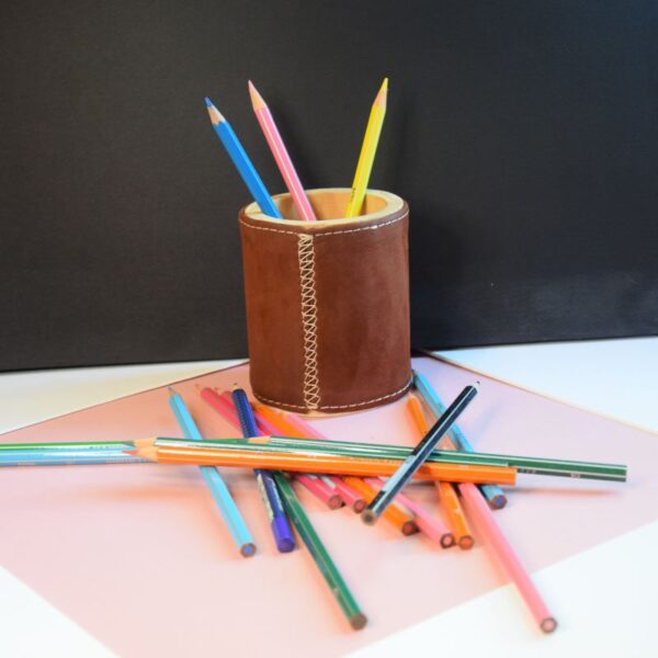 Cette photo représente un étui à crayon en bois recouvert de cuir velours marron. Des crayons sont posés à côté