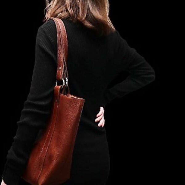 Cette image représente une jeune femme portant un grand sac en cuir marron avec 2 anses